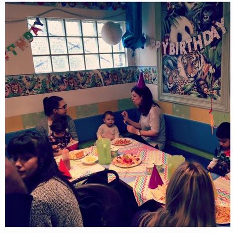 Children and parents at a long party table with food and birthday banners